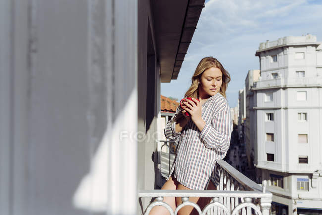 Joven mujer alegre con taza en la terraza - foto de stock