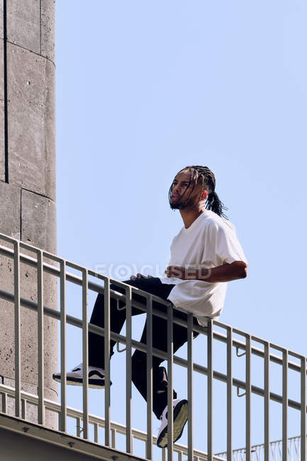 Молодий афроамериканець чоловік, сидячи на перил мосту на міській вулиці в сонячний день — стокове фото