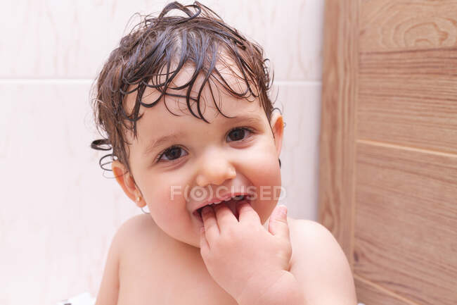 Забавна дитина дивиться на камеру і смокче пальці під час миття у ванній вдома — стокове фото