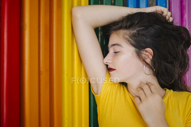 Pretty young female in casual outfit cheerfully closed eyes while lying on rainbow bench background — Stock Photo