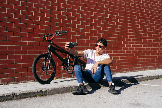 Jeune homme noir heureux prenant selfie avec smartphone près de vélo — Photo de stock