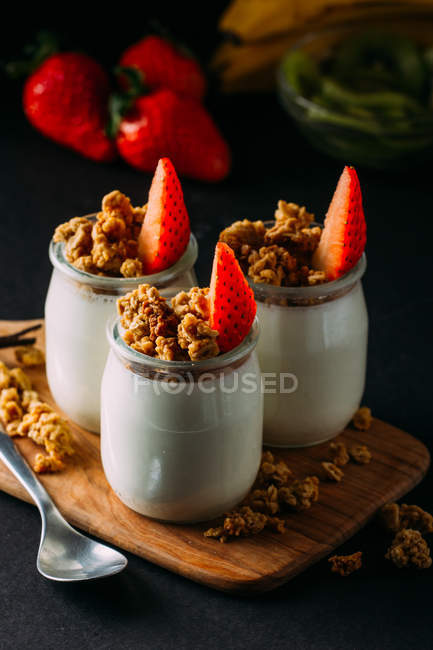 Glasses of cold tasty milk and delicious granola with spoon on wooden board — Stock Photo