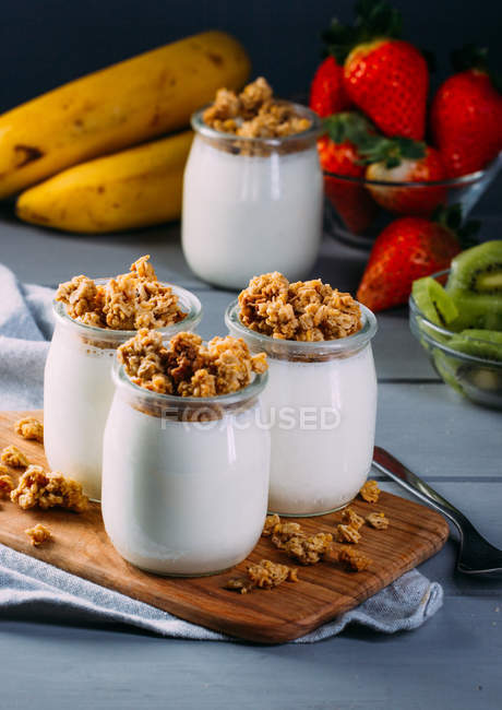 Óculos de leite saboroso frio e deliciosa granola com colher na tábua de madeira — Fotografia de Stock
