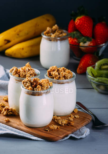 Glasses of cold tasty milk and delicious granola with spoon on wooden board — Stock Photo