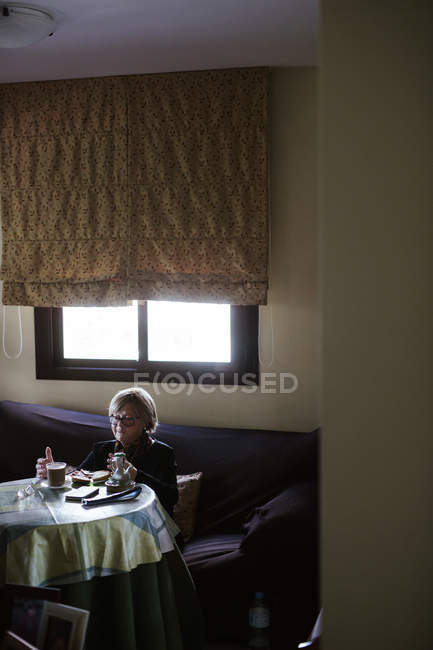 Зверху літня жінка снідає сидячи за столом — стокове фото