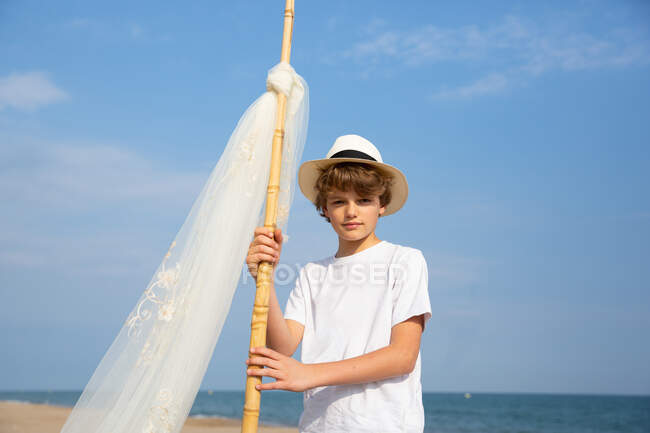 Niño en sombrero adjuntando toldo en poste en la arena en la playa - foto de stock