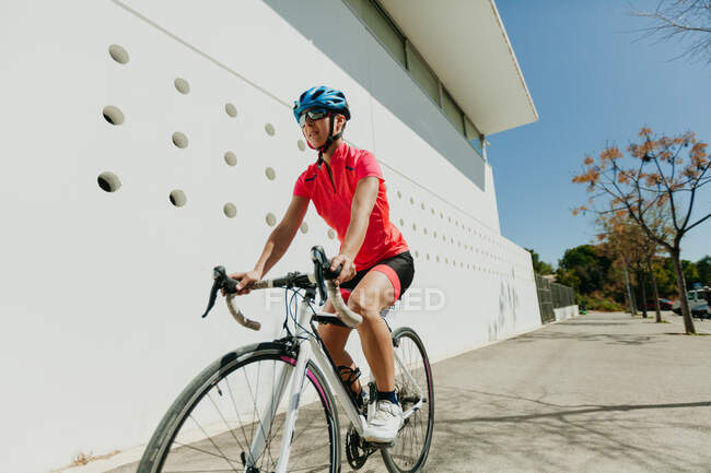Feminino no capacete e sportswear andar de bicicleta na rua da cidade no dia ensolarado — Fotografia de Stock