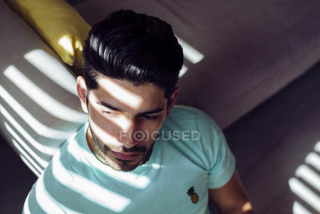 From above young tired depressed alone male in casual shirt sitting on sofa at home and looking at camera — Stock Photo