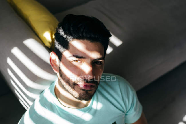 From above young tired depressed alone male in casual shirt sitting on sofa at home and looking at camera — Stock Photo