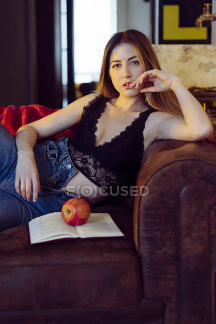 Молода сексуальна жінка сидить на дивані з яблуком і книгою — стокове фото