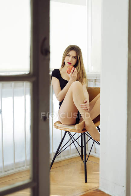 Молода спокуслива жінка з яблуком сидить на стільці — стокове фото