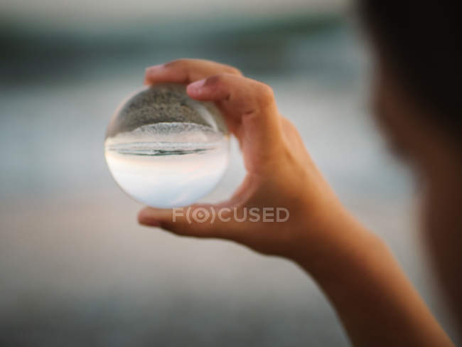 Primer plano de la mano del niño sosteniendo la bola de vidrio sobre el fondo de ondas borrosas - foto de stock