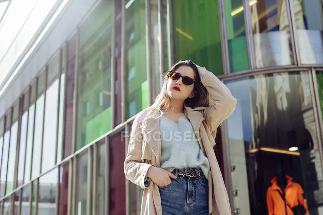 Jeune femme en lunettes de soleil et trench-coat posant dans la rue — Photo de stock