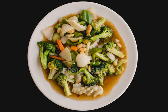 De arriba preparado la sopa sabrosa caliente con los calamares y hortalizas sanas, como el brócoli, la zanahoria, la cebolla, el pepino sobre el fondo negro - foto de stock
