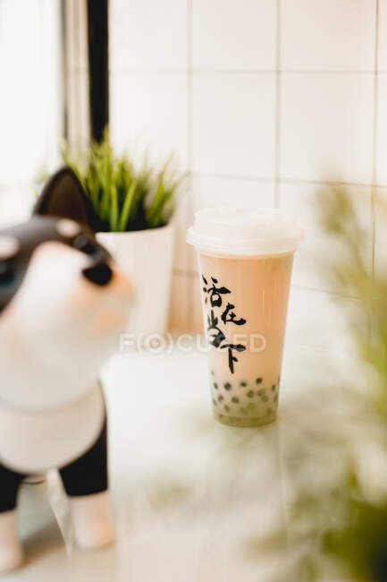 Вкусный чай с пузырьком молока с жемчугом тапиока в пластиковой чашке на столе возле горшечных растений в традиционном тайваньском кафе — стоковое фото