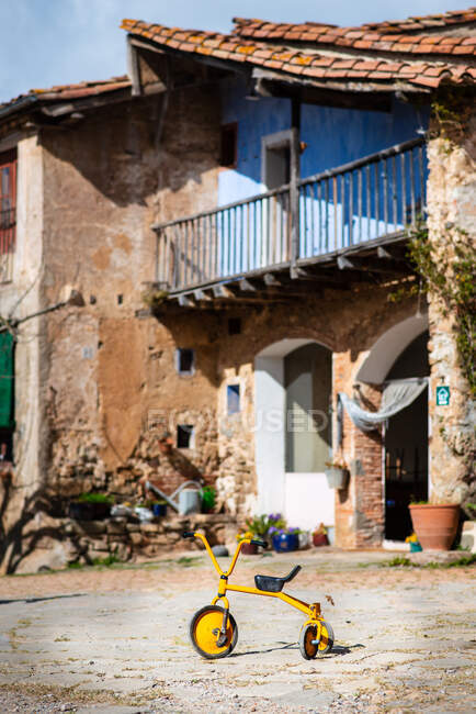 Діти яскраво-жовтий красивий велосипед на дорозі біля стародавнього сільського будинку з пілінговою фарбою — стокове фото