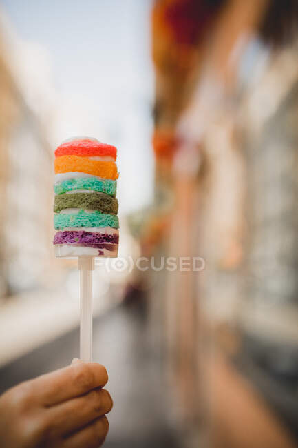 Tenendo in mano cotto gustoso dolce torta arcobaleno e camminare sulla strada della città — Foto stock