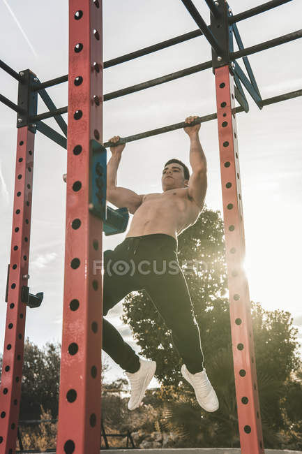 Shirtless young guy performing pull ups on bar during workout on city street on sunny day — Stock Photo