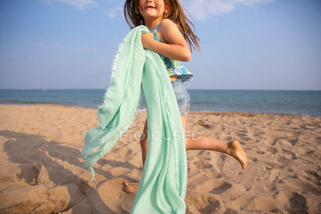 Усміхнена дівчина з довгим волоссям в літньому повсякденному одязі тримає тонку тканину парео в сонячний день — стокове фото