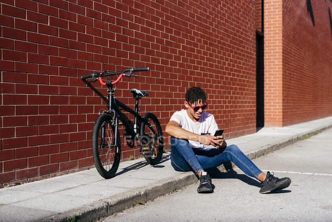 Молодой счастливый черный мужчина просматривает смартфон на велосипеде — стоковое фото