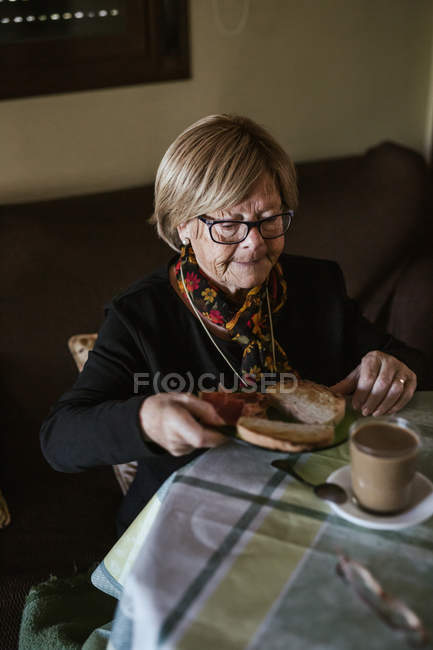 Зверху літня жінка снідає сидячи за столом — стокове фото