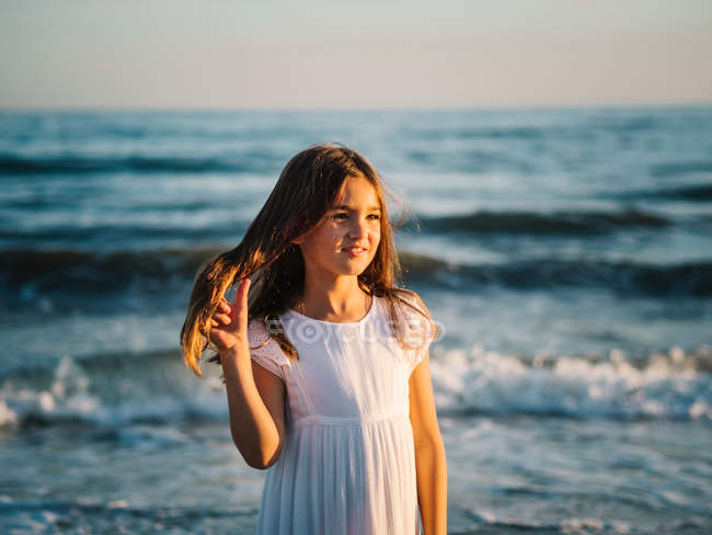 Little girl in white dress standing on background of evening sea — Stock Photo