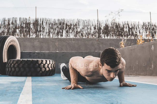 Мускулистый молодой парень делает отжимания во время тренировки на бетонном полу спортивной площадки на городской улице — стоковое фото