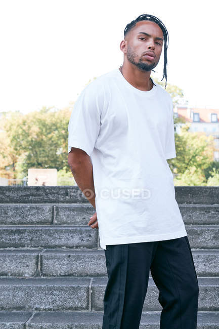 Confident African American male in casual outfit looking at camera while standing on steps on city street — Stock Photo