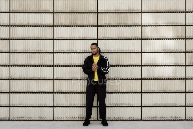 Jeune homme afro-américain en vêtements de sport à la mode regardant la caméra tout en se tenant près de blocs de ciment sur la rue de la ville — Photo de stock