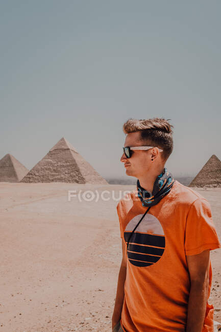 Viajante masculino confiante em óculos de sol olhando para longe enquanto estava no deserto contra as famosas Grandes Pirâmides no Cairo, Egito — Fotografia de Stock