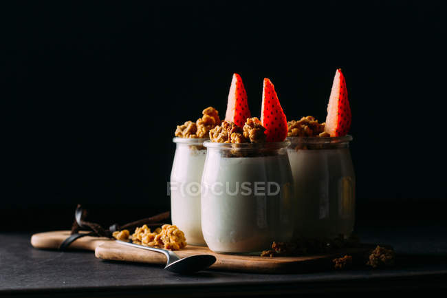 Óculos de leite frio saboroso e deliciosa granola com morangos em tábua de madeira sobre fundo preto — Fotografia de Stock