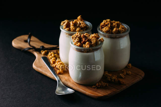 Óculos de leite saboroso frio e deliciosa granola em placa de madeira no fundo preto — Fotografia de Stock