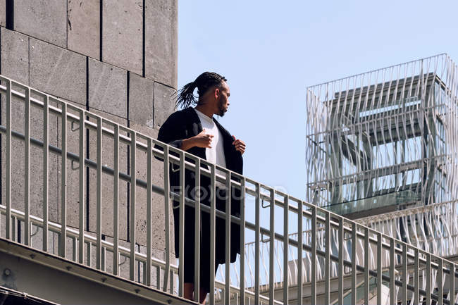 Young African American man leaning on railing of bridge on city street on sunny day — Stock Photo