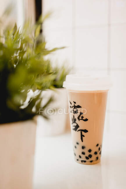 Saboroso chá de bolha de leite com pérolas de tapioca em copo de plástico na mesa perto de plantas em vasos no tradicional café taiwanês — Fotografia de Stock