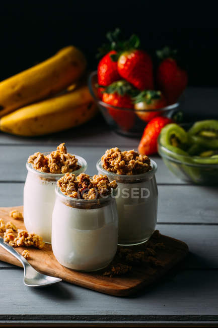Óculos de leite saboroso frio e deliciosa granola com colher na tábua de madeira — Fotografia de Stock