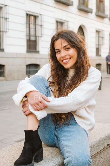 Pretty young female in casual outfit smiling and looking at camera on city street — Stock Photo