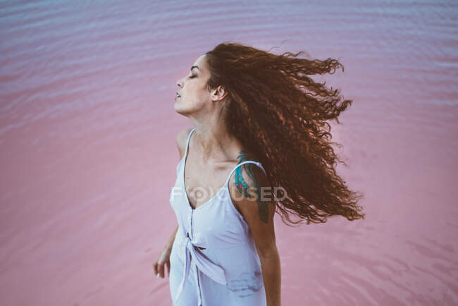 Молодая красивая женщина с длинными кудрявыми волосами в летнем платье наслаждаясь морским бризом — стоковое фото