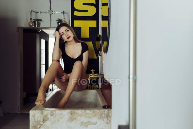 Jeune femme sexy en lingerie posant sur le bain dans la salle de bain — Photo de stock