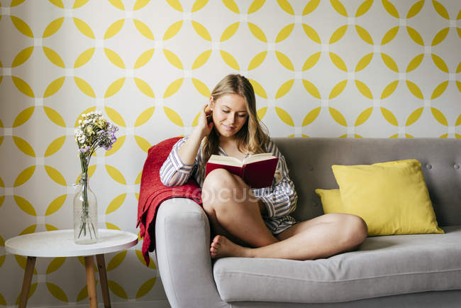 Jovem mulher feliz ler livro no sofá — Fotografia de Stock