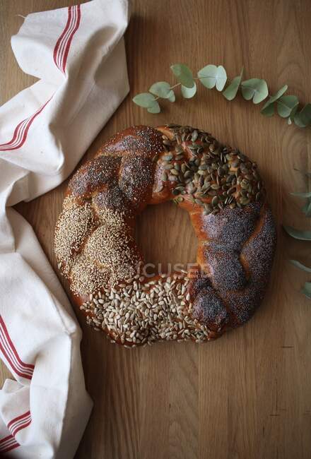 Yummy fresh challah bread with various seeds placed on lumber tabletop near cloth napkin and green plant sprig — Stock Photo