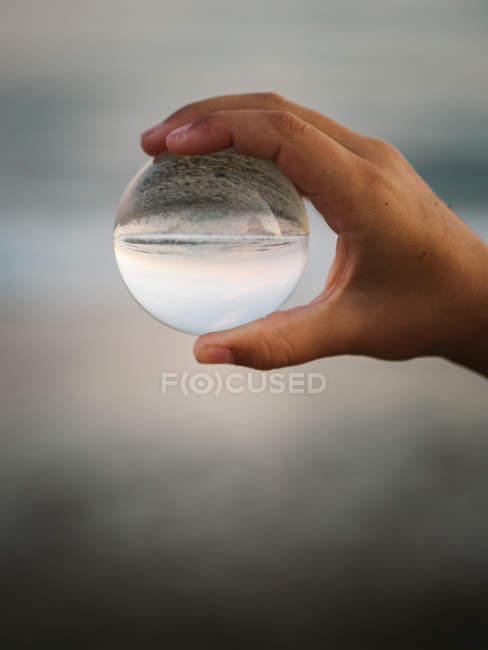 Крупним планом рука дитини, що тримає скляну кульку на тлі розмитих хвиль — стокове фото