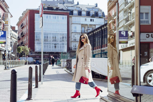 Giovane donna alla moda in trench e occhiali da sole a piedi in città — Foto stock