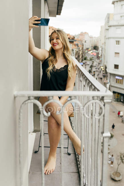 Молодая улыбающаяся женщина делает селфи на террасе — стоковое фото