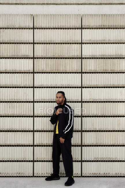 Junger afrikanisch-amerikanischer Typ in trendiger Sportbekleidung blickt in die Kamera, während er in der Nähe von Betonblöcken auf der Stadtstraße steht — Stockfoto