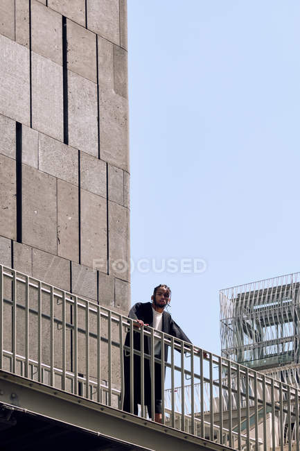 Молодий афроамериканець чоловік, спираючись на перила мосту на міській вулиці в сонячний день — стокове фото