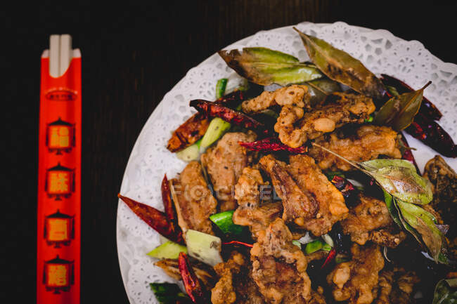 Сверху приготовленный аппетитный ягненок с огурцом, перец чили и листья на тарелке с палочками в азиатском кафе — стоковое фото