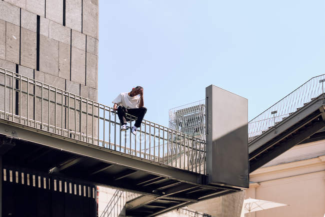 Giovane uomo afroamericano seduto sulla ringhiera del ponte sulla strada della città nella giornata di sole — Foto stock