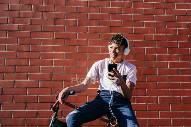 Giovane felice uomo nero ascoltare musica con smartphone in bicicletta — Foto stock