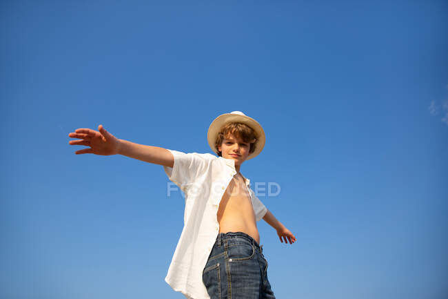 Desde arriba chico atractivo en sombrero y camisa desabotonada de pie con las manos abiertas - foto de stock