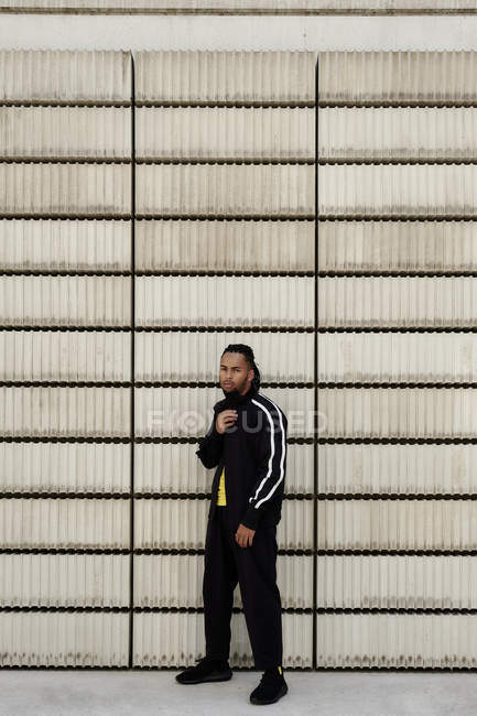 Giovane ragazzo afroamericano in abbigliamento sportivo alla moda guardando la fotocamera mentre in piedi vicino blocchi di cemento sulla strada della città — Foto stock